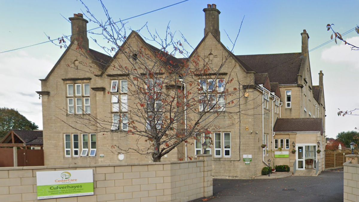 External shot of Culverhayes Nursing Home, which is a sand-coloured building. A wall with a sign saying ' Culverhayes' is on a surrounding wall.