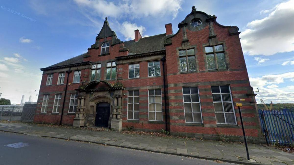 Street view of the large red brick Gothic looking two-storey building with tall windows.