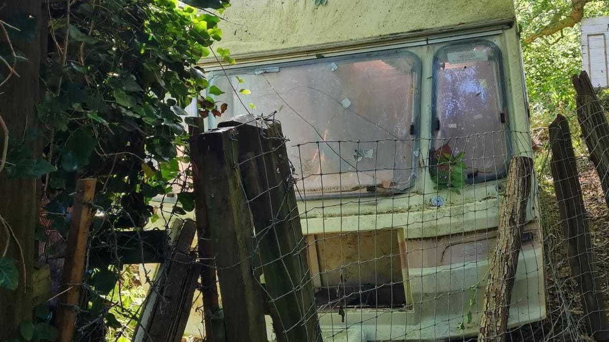 Old caravan next to fence in wooded area