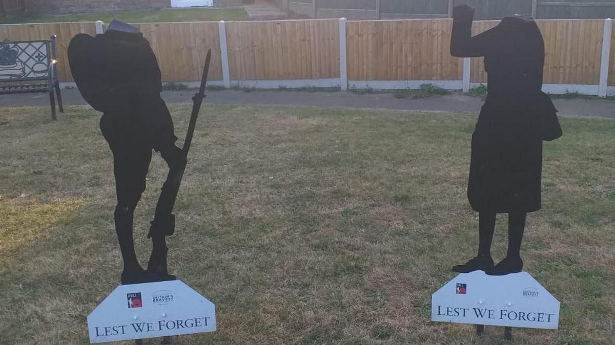 Image shows a Tommy silhouette and a Women in War silhouette neither of which have heads. They are on a lawn in front of a fence