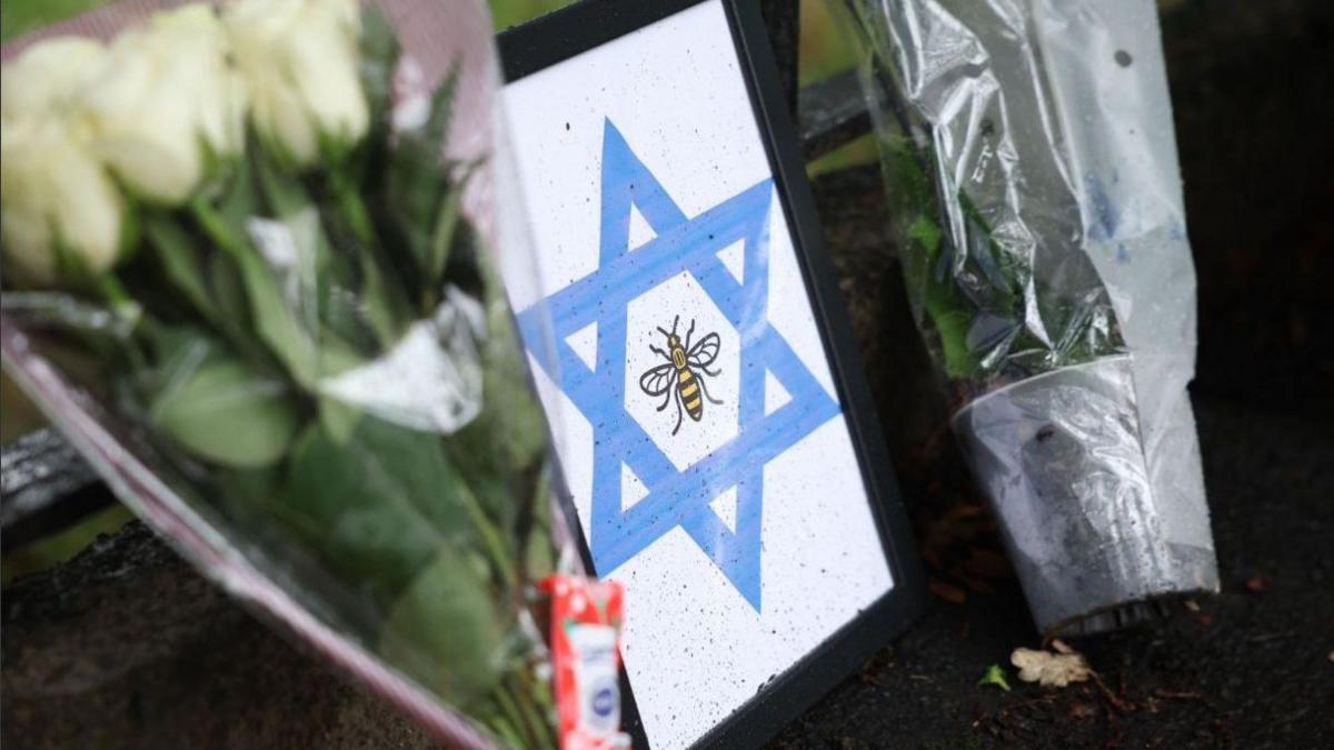 A framed Star of David with a bee, the symbol of Manchester, is left at the scene of a deadly terror attack in Manchester. Bunches of lowers have also been left on either side of the picture. 