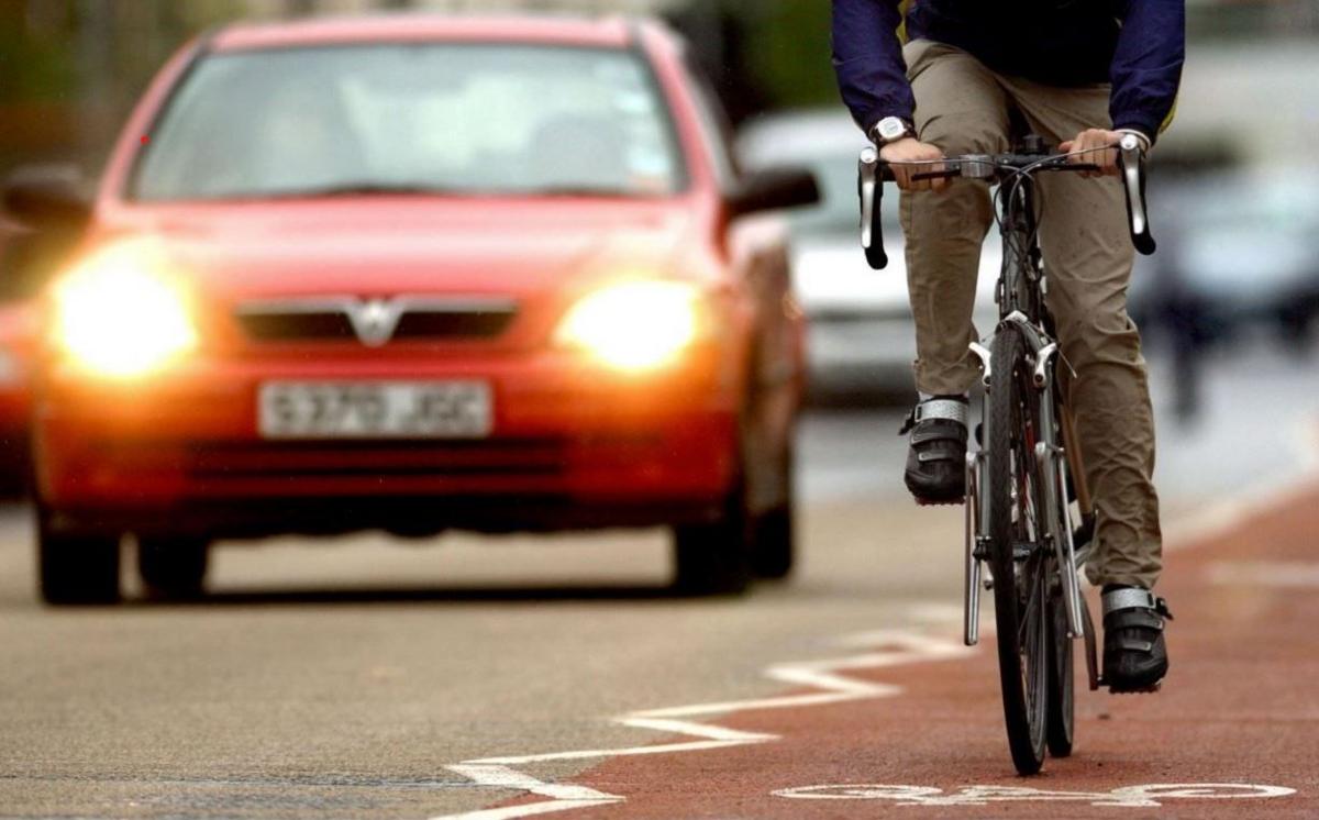 An anonymous cyclist is in a cycle lane on a main city road, as cars pass him on his right