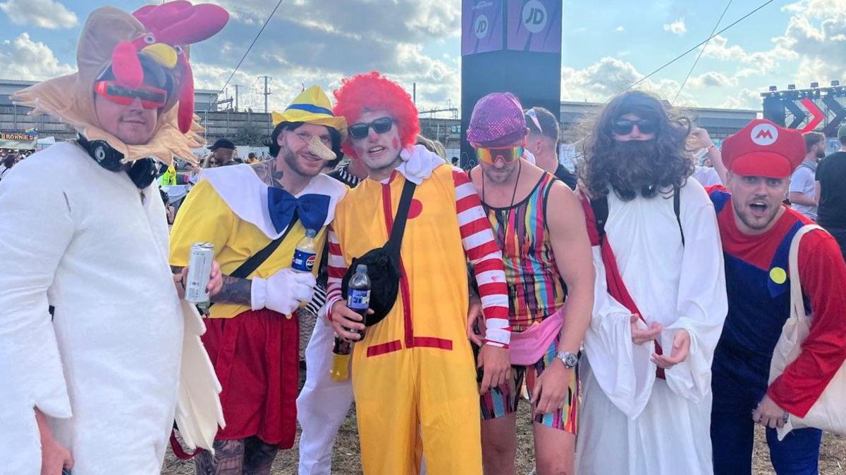 Six men wearing fancy dress. There is a chicken, Pinocchio, Ronald MacDonald, Mister Motivator, Jesus and the videogame character Mario