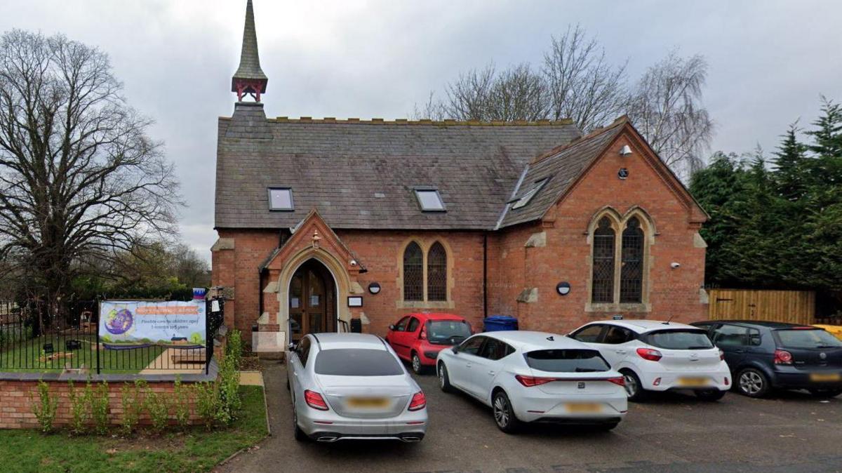 A brick building with a grey roof and cars parked at the front.