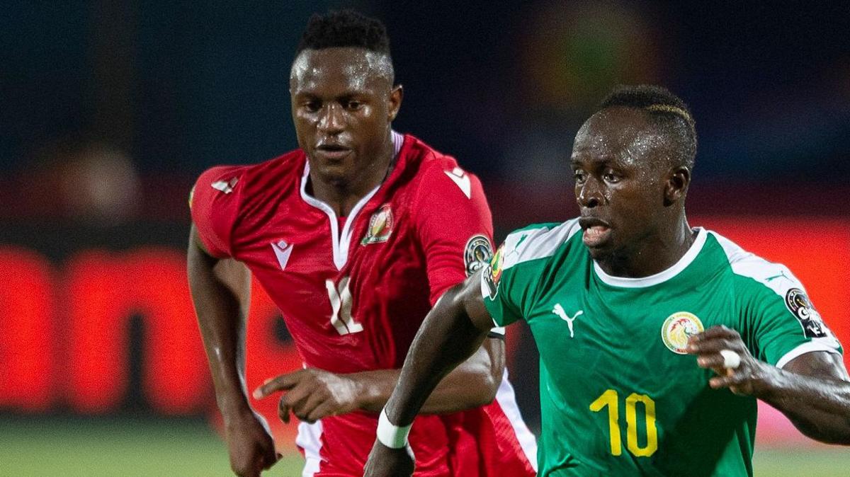 Victor Wanyama and Sadio Mane are seen in red and green shirts respectively as the players run towards the camera during an international football game between Kenya and Senegal