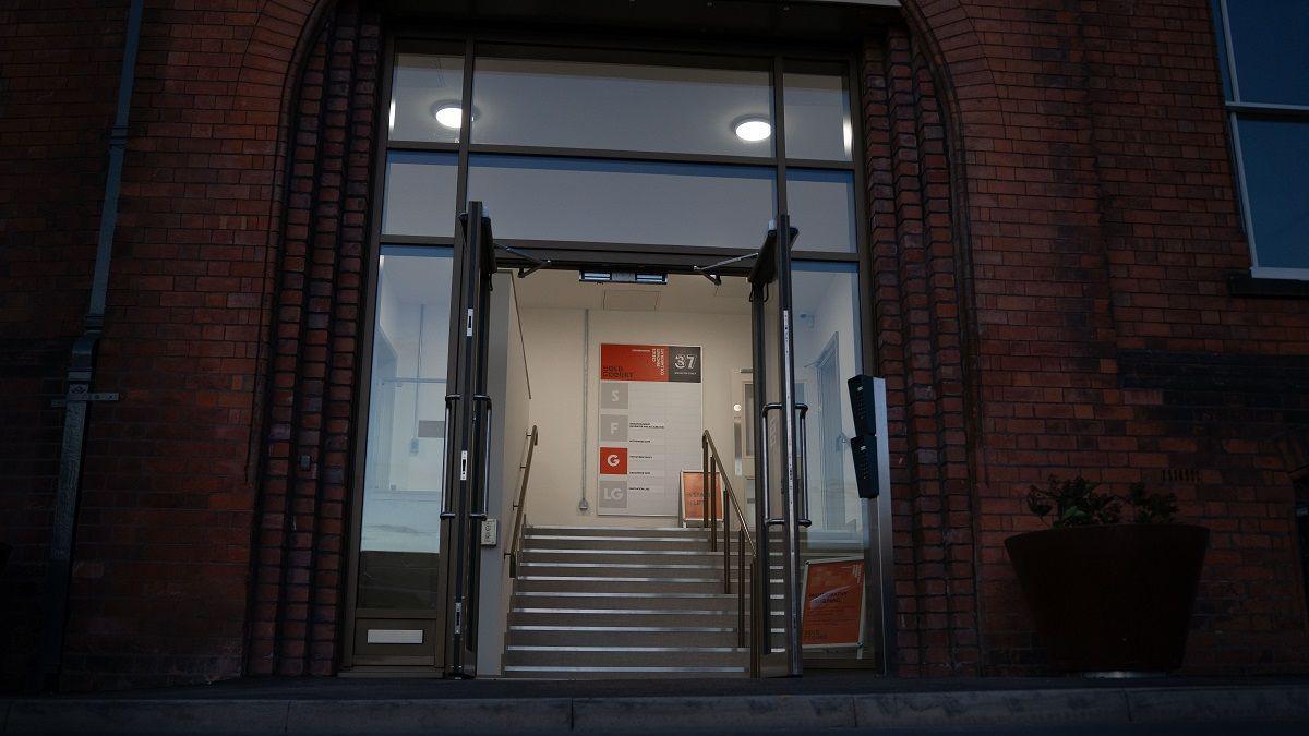 A dark shot of the entrance to a building. It is a former court and has red brick. But there are modern doors. There are stairs and signs on the wall telling visitors where to go. 