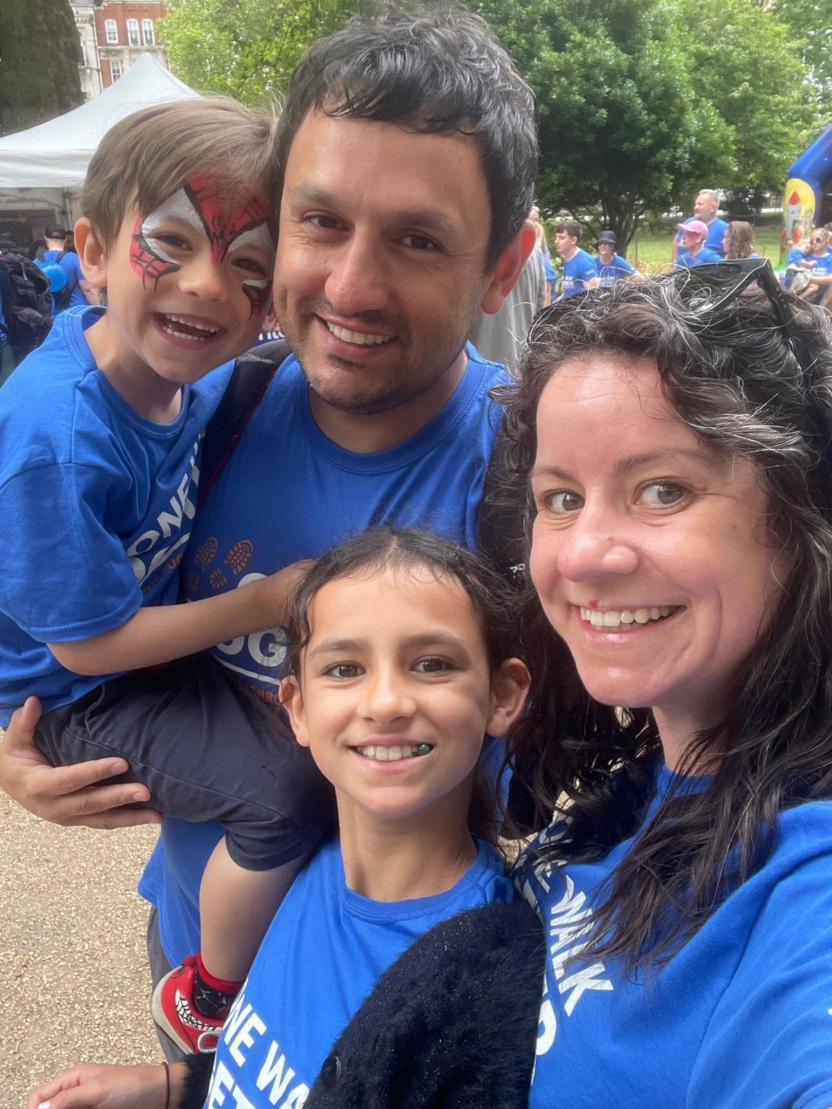 Theo Sebastian-Jenkins is being carried in the arms of his father Ben. His sister and mother, Vicky, are also in shot. It's a selfie-style photo with all four looking at the camera and wearing blue charity t-shirts.