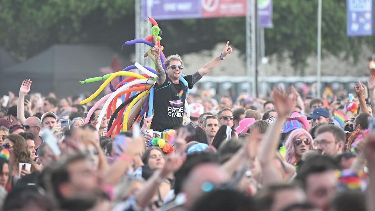 Crowd of people with one man on someone's shoulders in a black t-shirt that says Pride Cymru