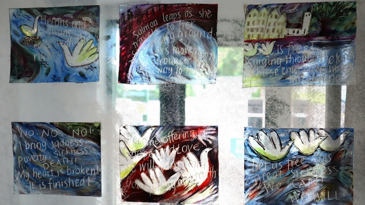 A series of glass panels which have been created by artists. There are birds and swans drawn on water which are covered in white writing.