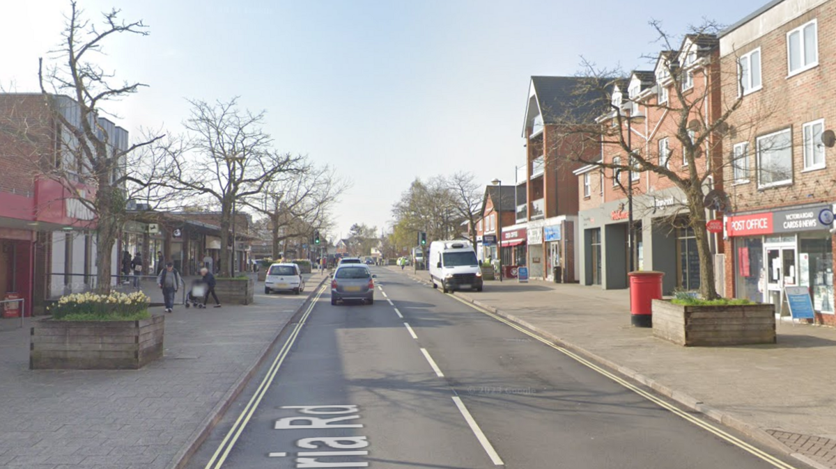 A screenshot from Google street view showing a road with wide pavements on either side. On the pavements are planters full of daffodils with trees in the middle.