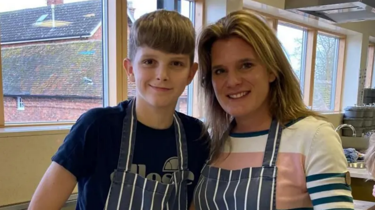 A woman stands with a young boy. They are both wearing aprons and are smiling.