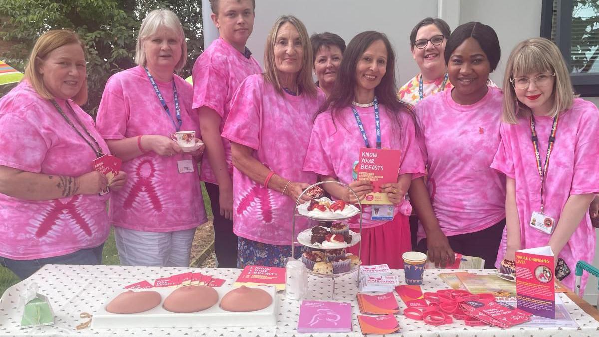 Attendees pose in pink T-shirts in front of an afternoon tea display