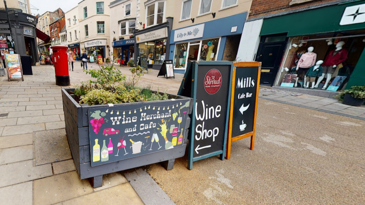 A picture of Stroud High Street showing shops and cafes and flower planters