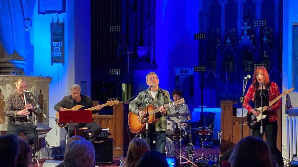 Glen Matlock and three other musicians perform with Kevin Brennan when he was an MP in St John's Church in Canton, Cardiff. The background is lit blue