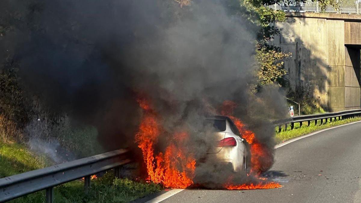 Car on fire on side of motorway, with large flames covering the vehicle