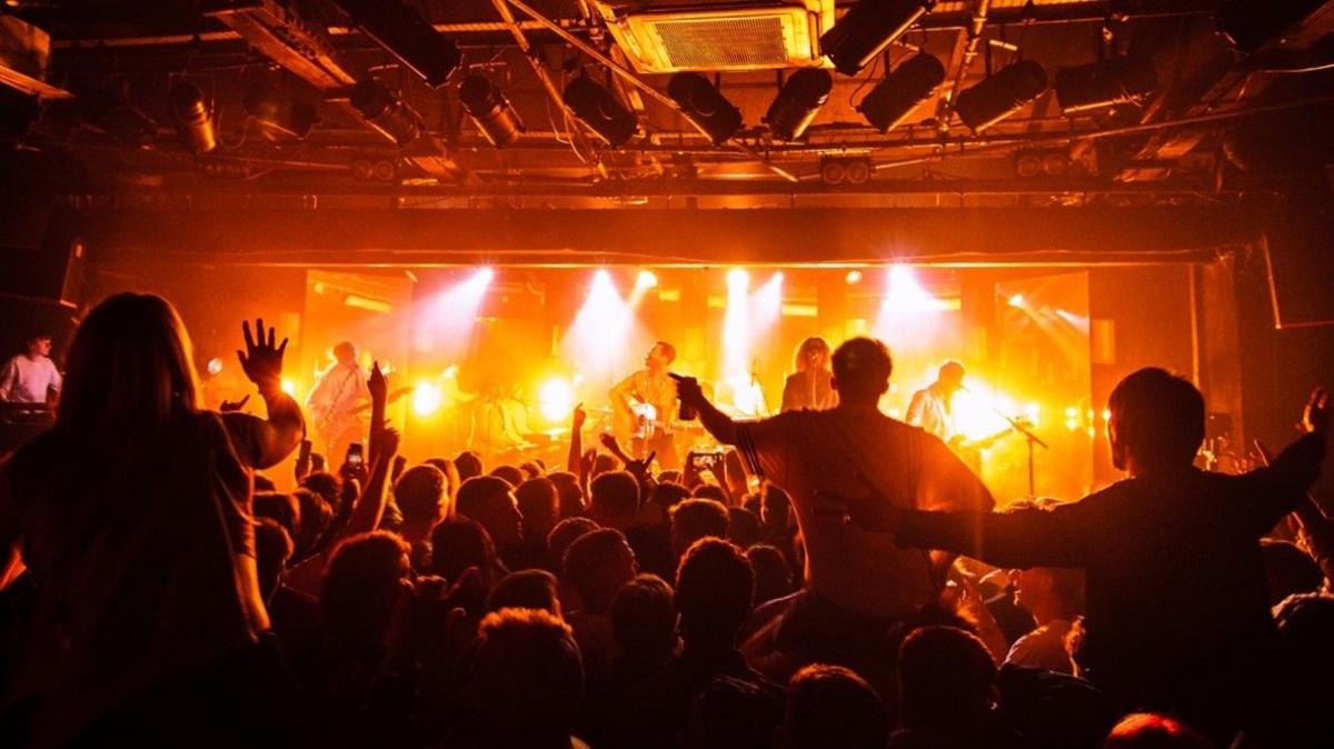 A general view from the back of the Leadmill music venue. A man, Miles kane, is on stage in the distance and a crowd with people dancing and sitting on each others shoulders is lit under orange lights