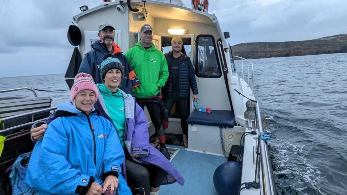 Five swimmers on the support boat. All smiling on deck.