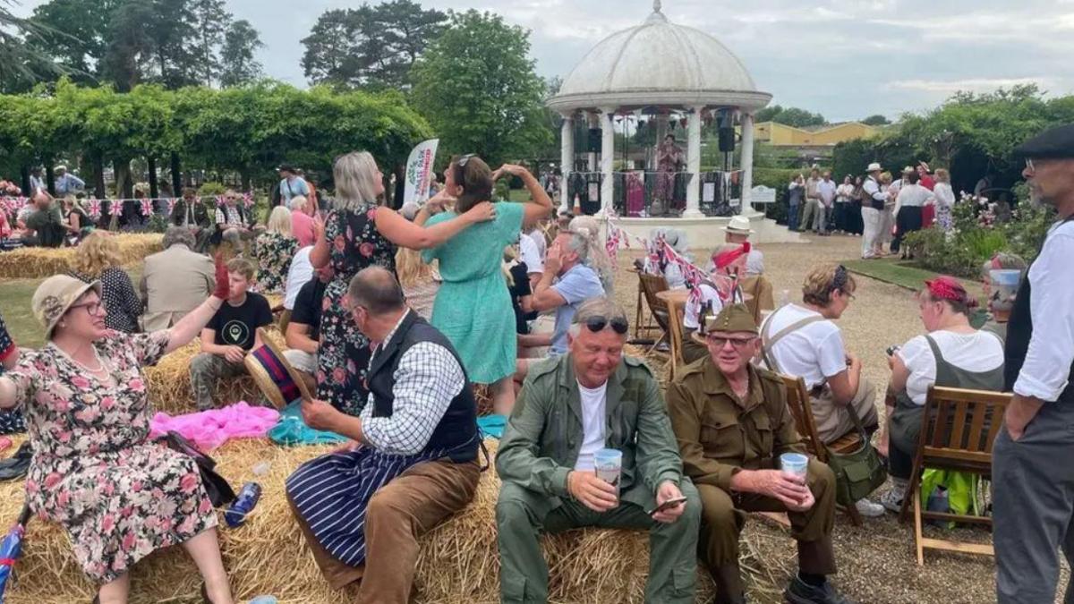 A group of people dressed in 1940s outfits sat on straw bales. 