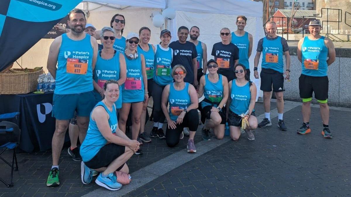 A group of runners pose at the end of the Bristol Half Marathon. They are a mixture of men and women and are all wearing light blue tops with St Peter's Hospice written on them