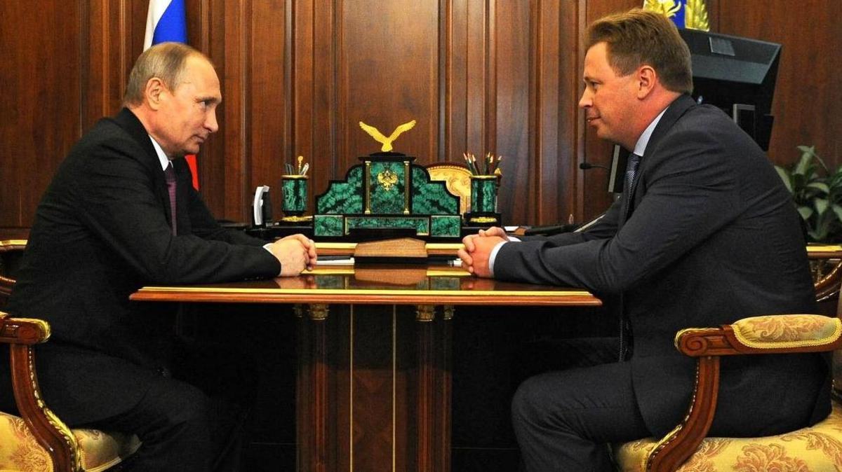 Vladimir Putin sits at a table across from Dmitrii Ovsiannikov, both have their hands clasped in front of them