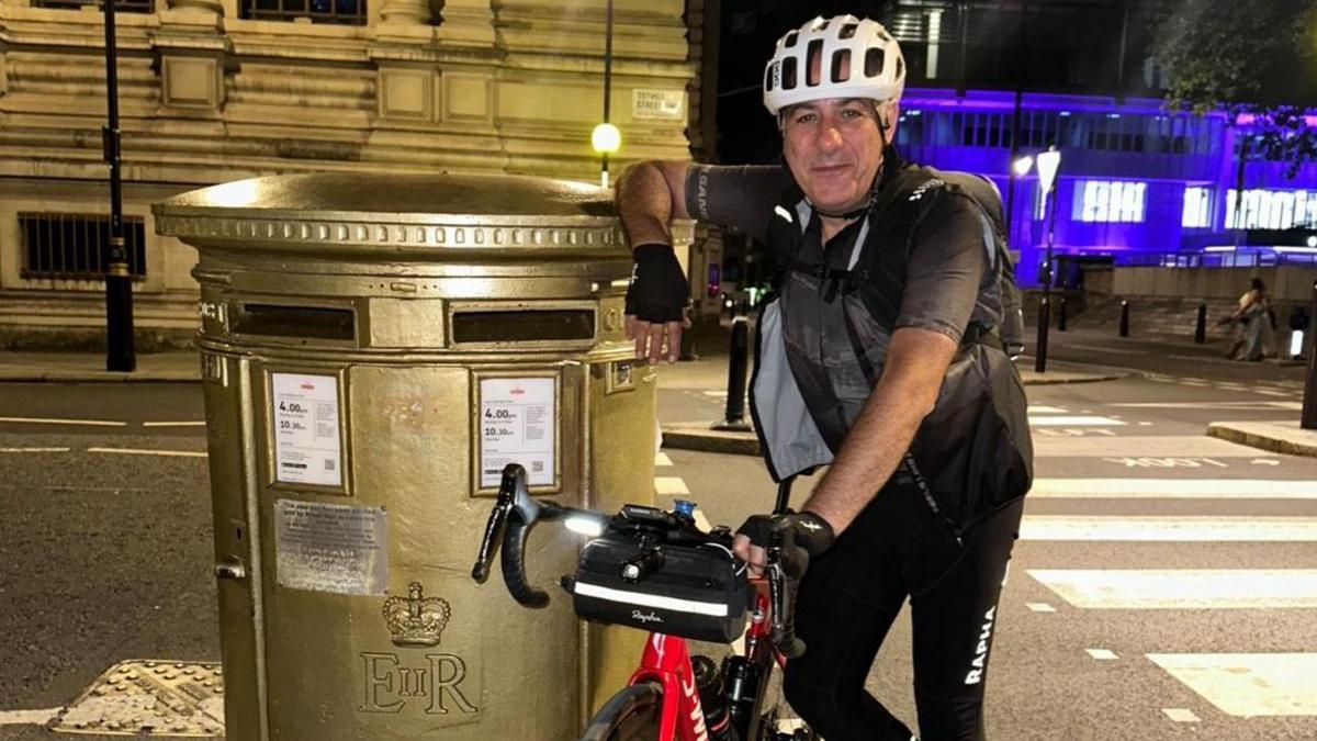 Nico Georgiou standing next to a gold letter box with his bike