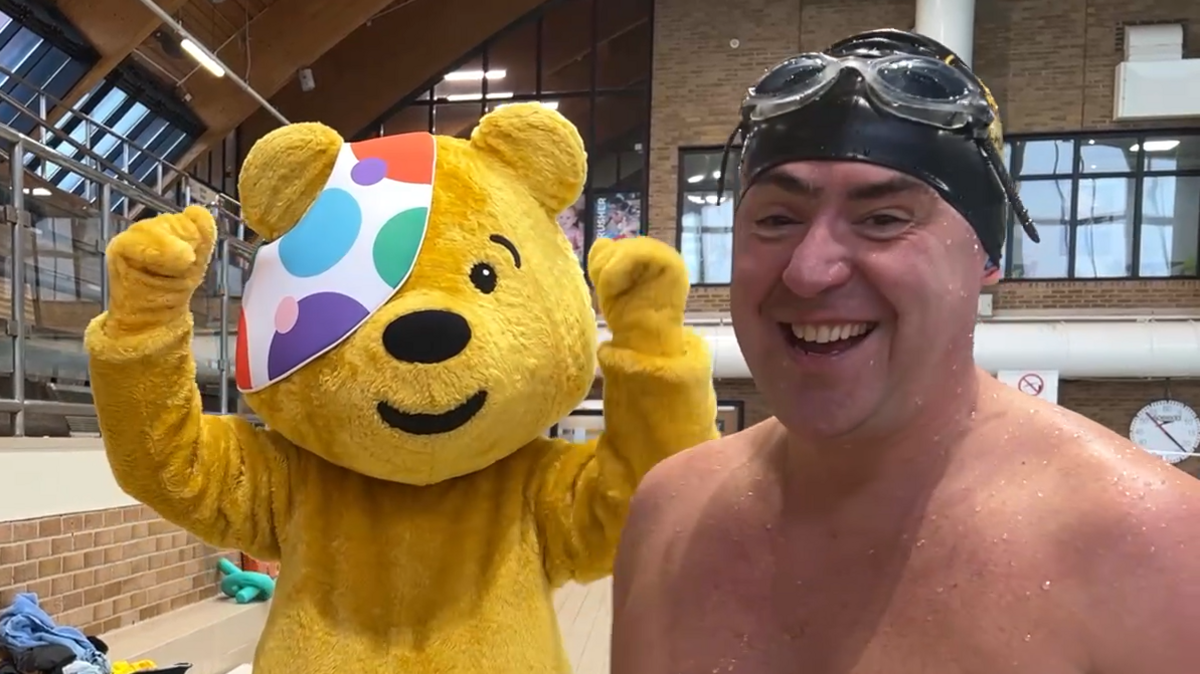 Pudsey, a human-sized yellow bear mascot wearing a patch over his eye, stands with his arms in the air. Next to him is Edward Sault, a topless man wearing goggles and a swimming cap.