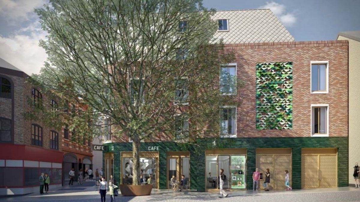 An artist's impression of a building shows a large tree in front of a cafe with green shop frontage on the ground floor and hotel rooms above it in a red-brick style.