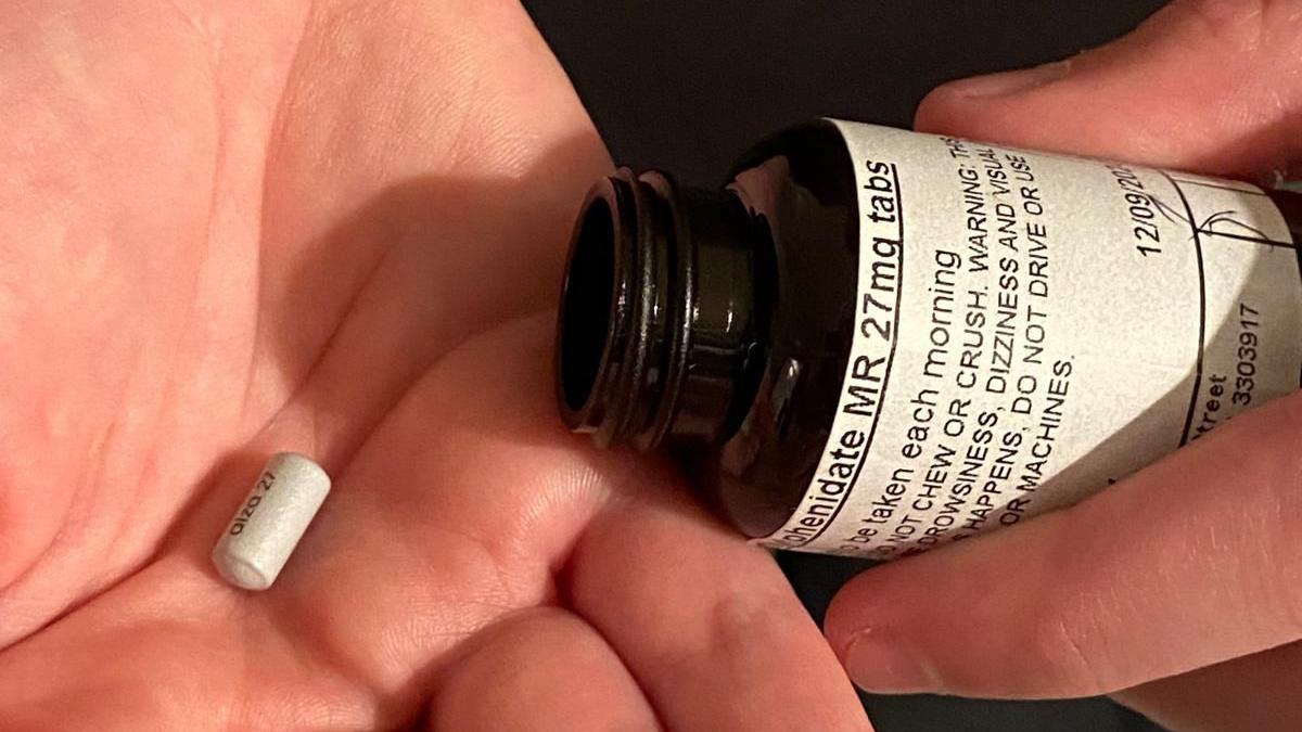 A pill in the palm of a hand with an open medicine bottle in the other hand