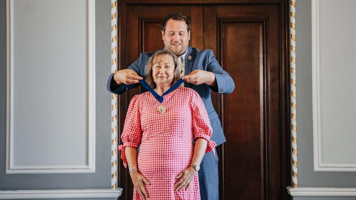 Rachel Nolan is awarded her vice-president medal by a man, she is wearing a red gingham dress