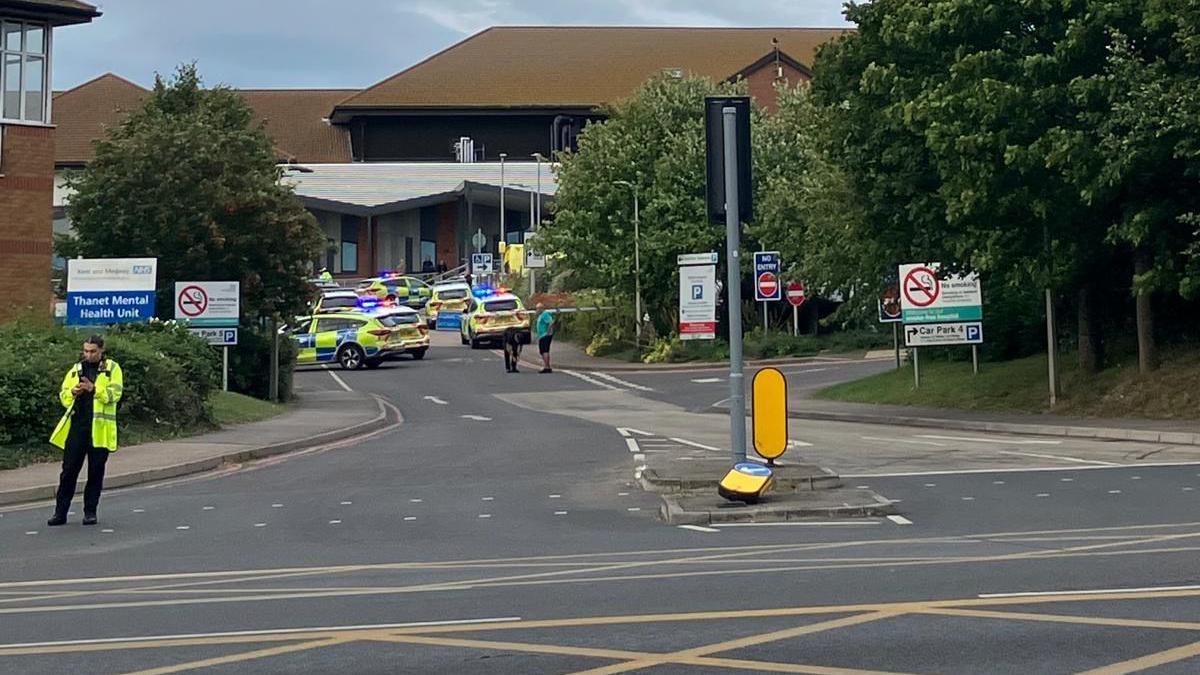 A number of police cars outside QEQM hospital in Margate , with several officers in hi-vis and blue and white incident tape across the entrance to the car park.