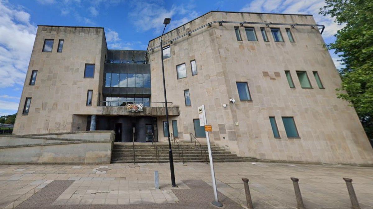 The exterior of Bolton Crown Court, with steps leading up to the main entrance and a bus stop sign outside.