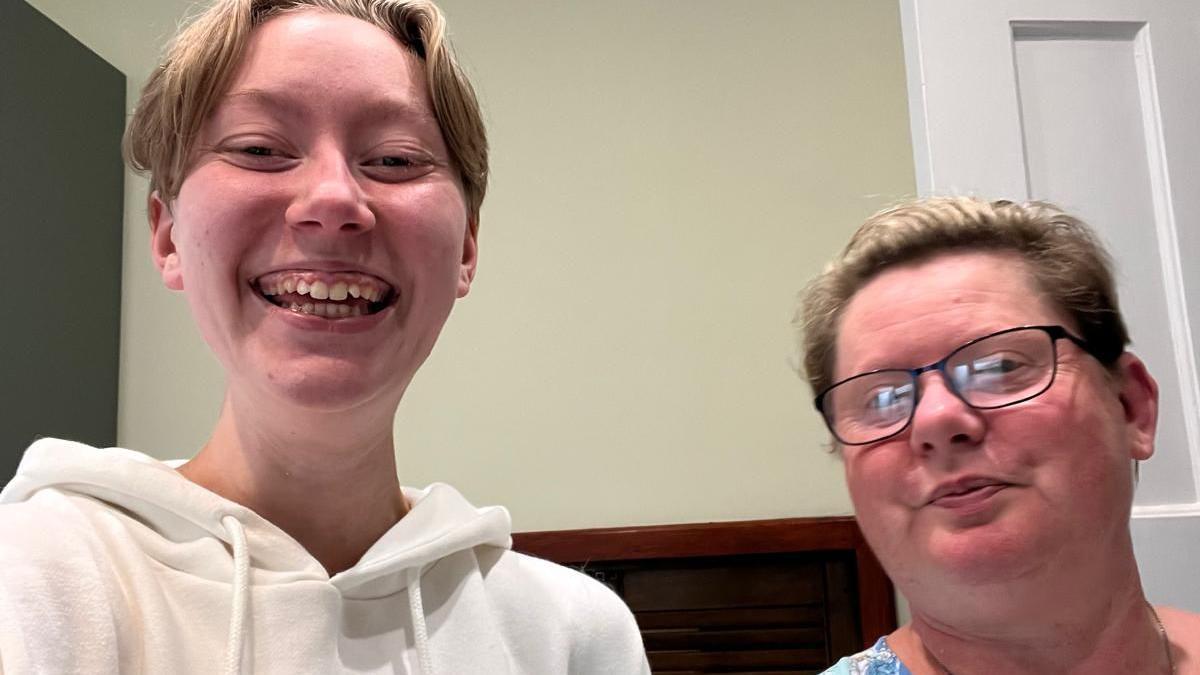 Chloe and Wendy smiling at the camera at home. Chloe has short blonde hair and Wendy has her hair tied back and is wearing dark rimmed glasses.