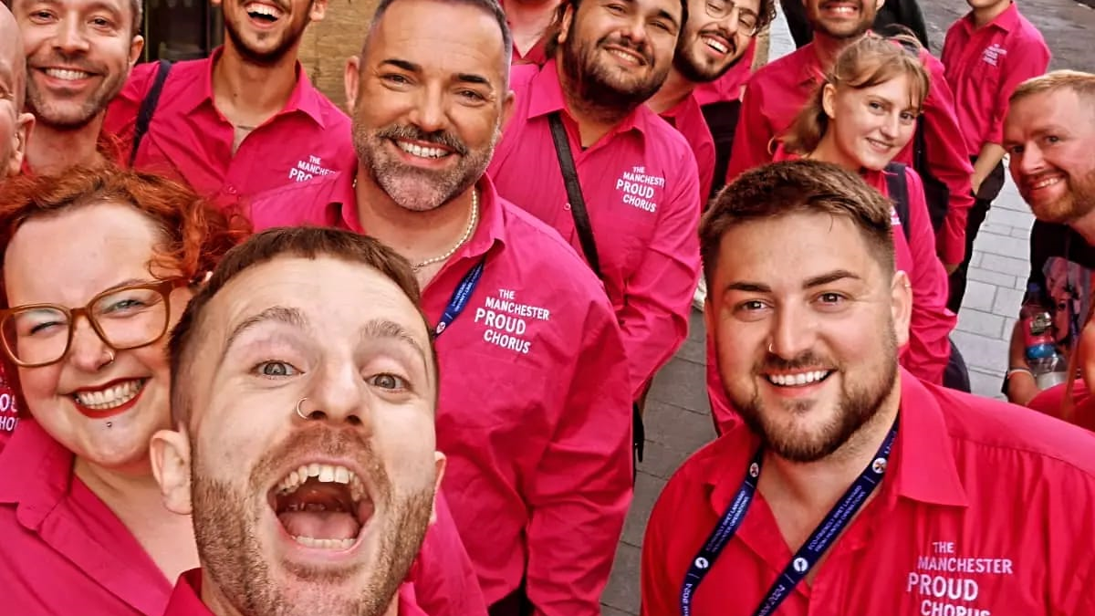 Members of the Manchester Proud Chorus choir pose for a photo wearing pink polo shirts emblazoned with the choir's name.