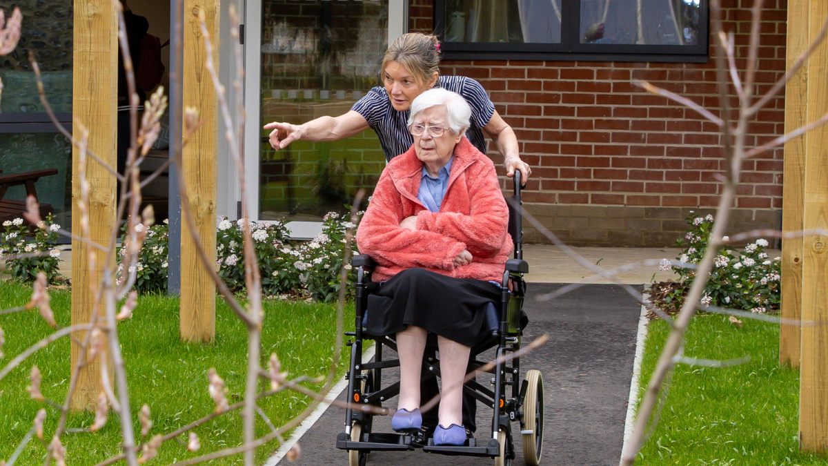 An elderly woman in a wheelchair being pushed by a younger woman