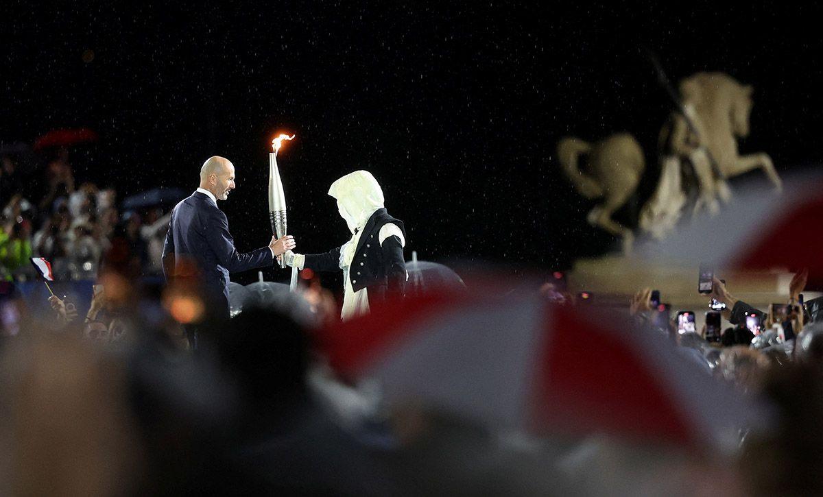 The torchbearer hands over the torch to former French footballer Zinedine Zidane at the Place du Trocadero during the opening ceremony of the Olympic Games