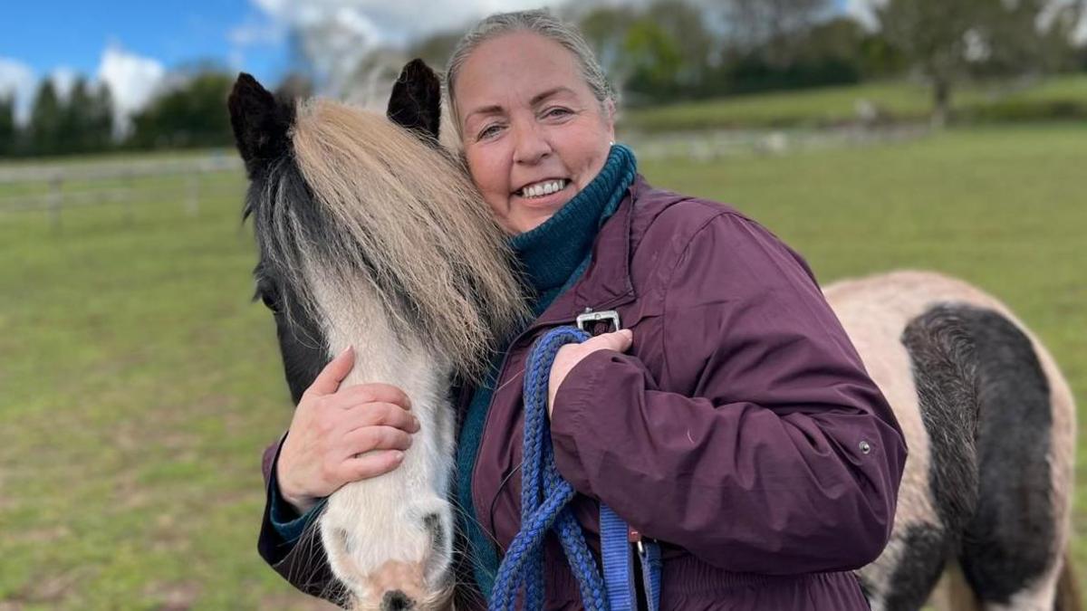 Alex is standing in a field, hugging a horse