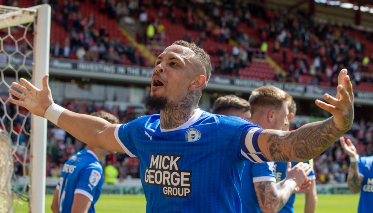 Peterborough United's Jonson Clarke-Harris celebrates after scoring a goal, with his arms outstretched.