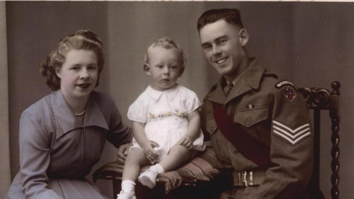 Michael, pictured as a baby seated between his father Donald - a man in military uniform to his left - and his mother - a woman in a blue dress seated to his right.