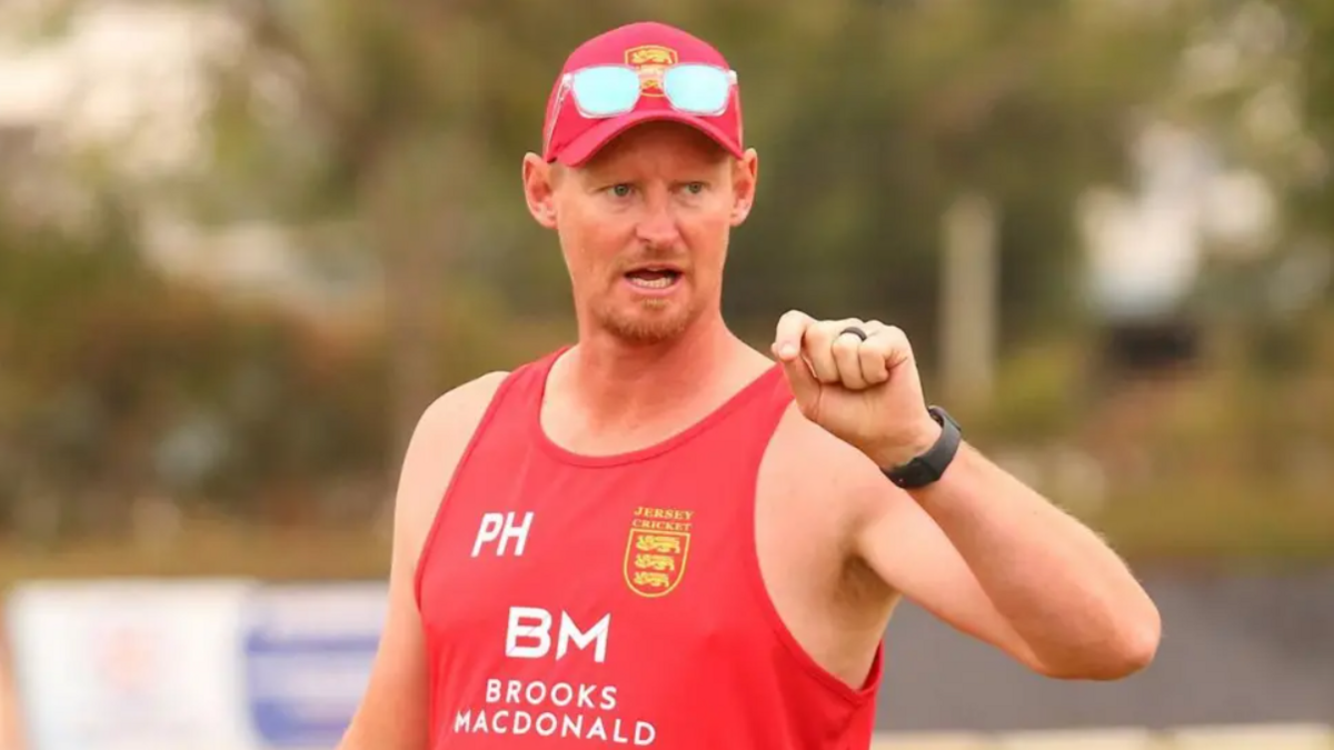 Paul Hutchinson wearing a red cap and red vest with the Jersey cricket crest on