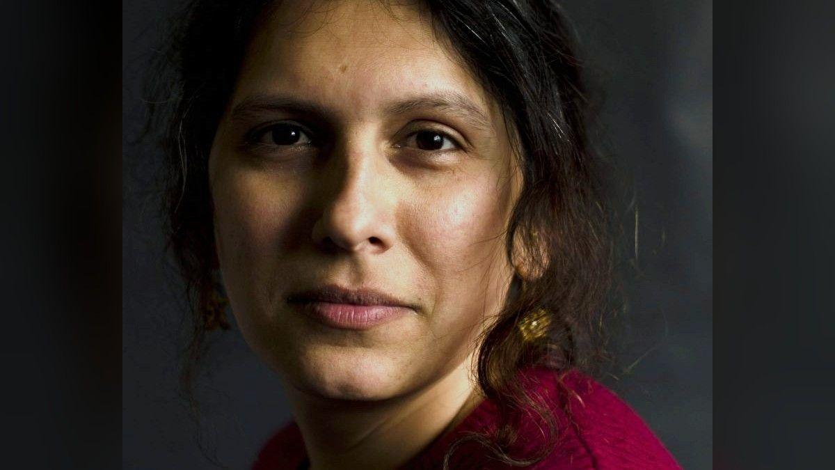 Mridul Wadhwa, a Scottish Indian trans woman with long brown hair and a magenta top, looks into the camera