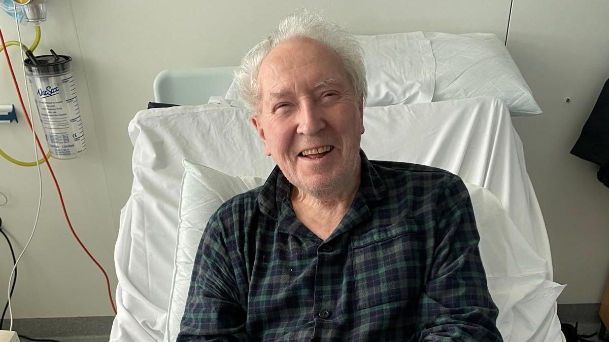 Man in a hospital bed smiling. 