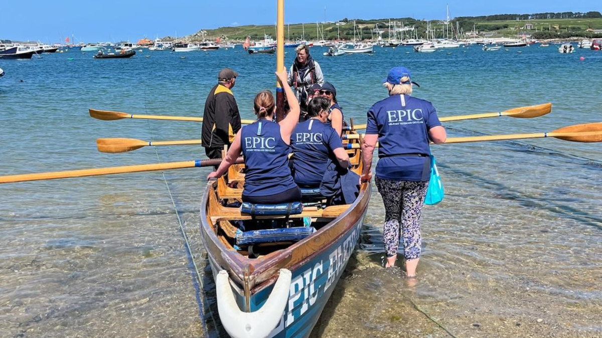 A team of rowers setting off from a sandy beach in a wooden gig boat.