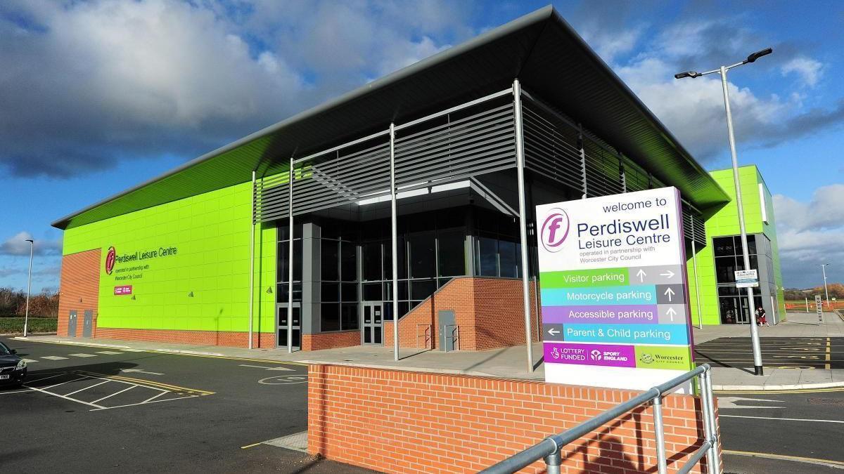 Bright green building with a low brick wall in front of it . There is a sign which details the visitor car park, motorcycle parking, and accessible parking