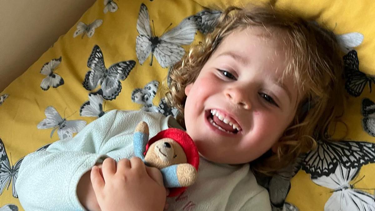 Alara lying on her bed cuddling her paddington bear comforter toy. She is smiling at the camera