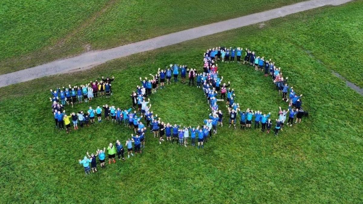 In this drone photograph, the number 500 is spelled out using runners and volunteers of the parkrun, all dressed in blue. Surrounding them is the grassy field and a path runs just above the 500.