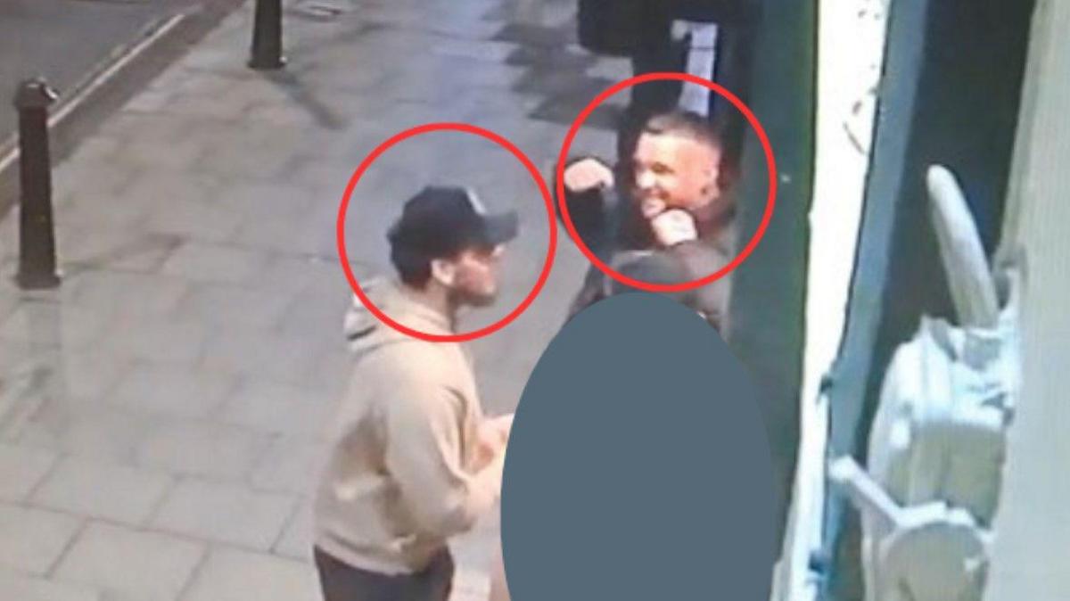 Two men are in the image and a red circle is around each head. They are standing on a pavement.