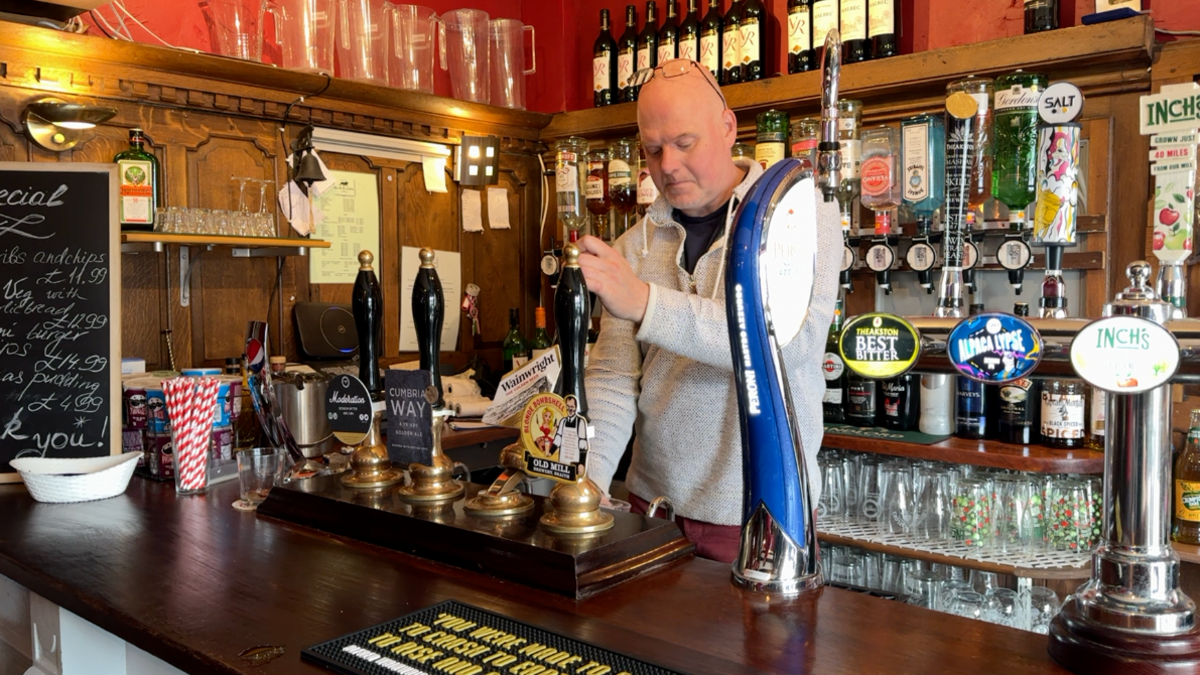 Mark Nellist, who has a shaved head, stand behind a bar pulling a pint.