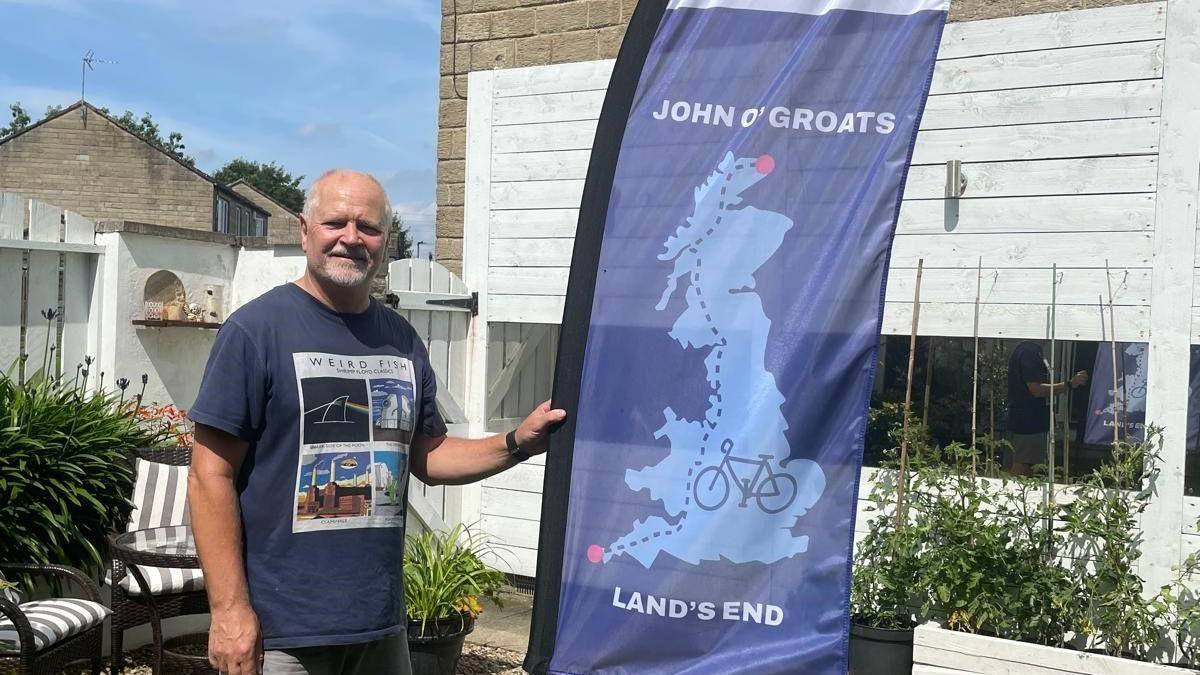 Eric Oakley poses with a flag detailing the Lands End to John O'Groats route