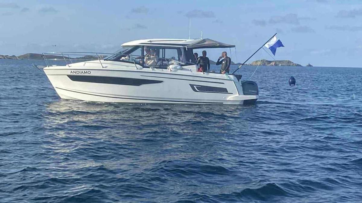 Swimmers in wetsuits can be seen on the stern of a small white support boat which has the name Andiamo written on the side.