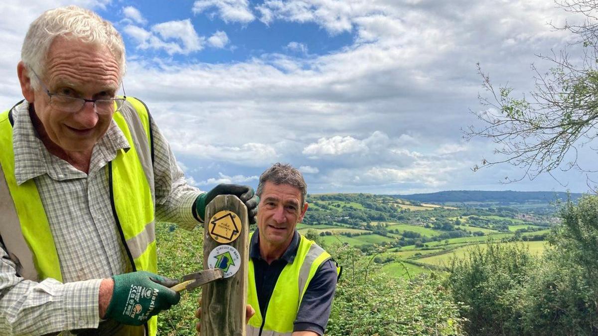 Two men working on a wooden post in the woodlands